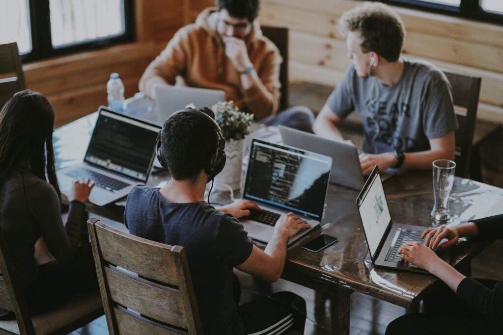 Five students working at same table on laptops.